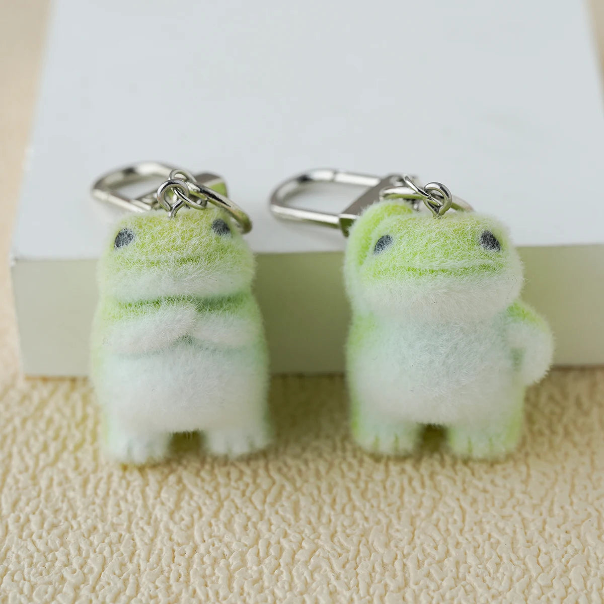 Two tiny plush emotional‑support frog keychains with soft green gradient fuzz and gentle little guy vibes, sitting together like portable comfort creatures.