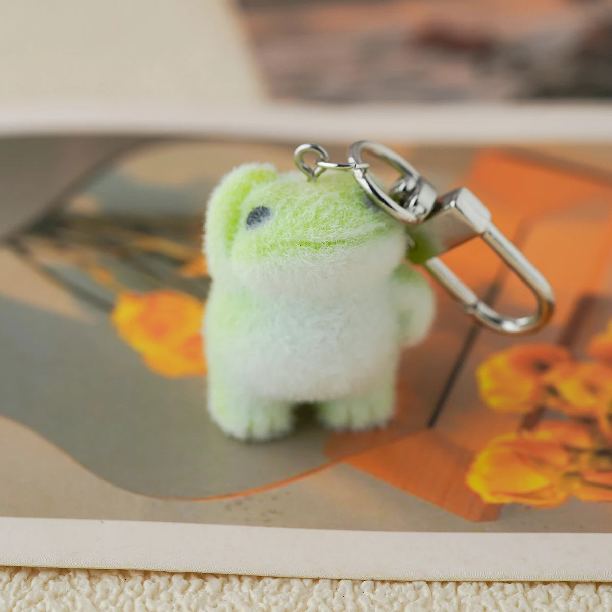 A tiny plush emotional‑support frog keychain with soft green fuzz, with one hand on his head like a little guy awaiting adoption